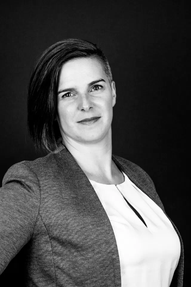 Schwarzweiß-Porträt von Ina Roth: kurze dunkle Haare, grauer Blazer, sie lächelt in die Kamera