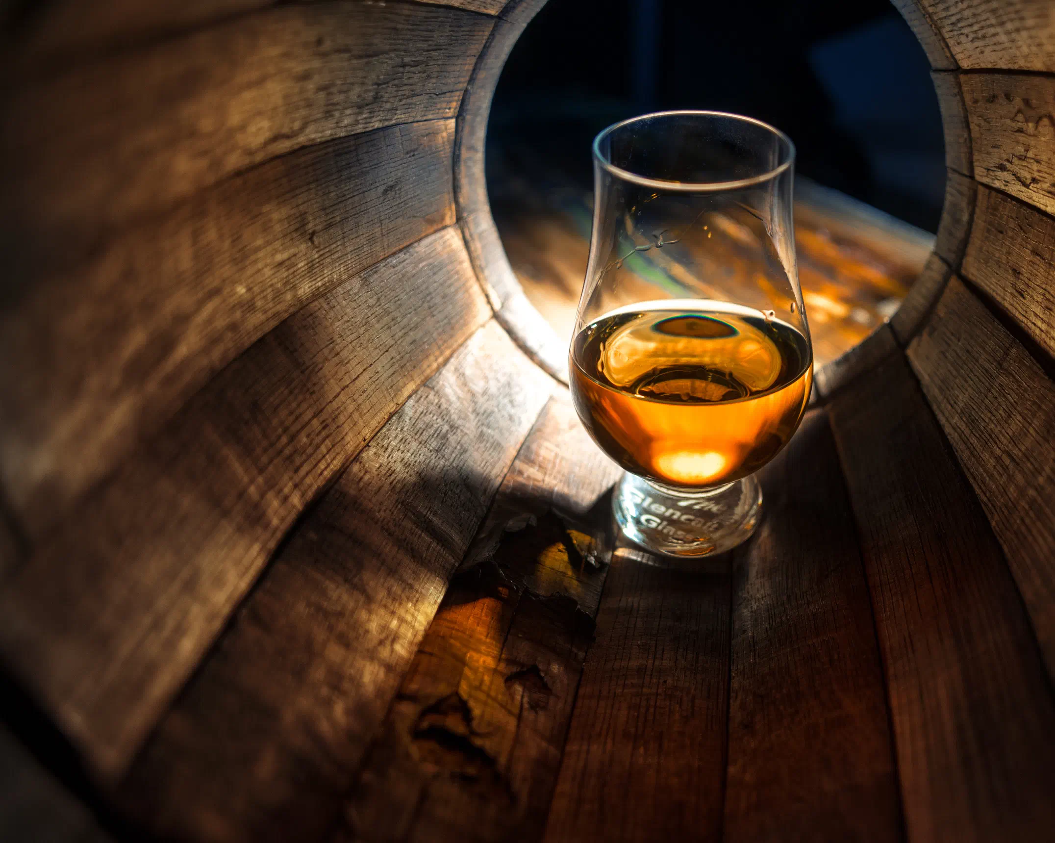 Ein Nosing-Glas mit Whisky, im Licht liegend in einem halben Holzfass